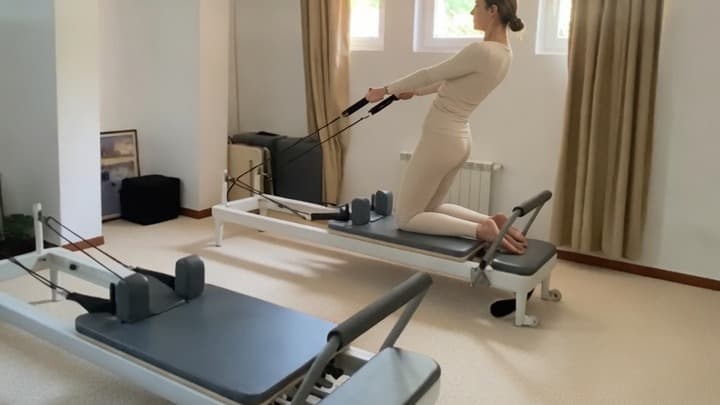 Clientă în genunchi pe reformer, trăgând de chingi