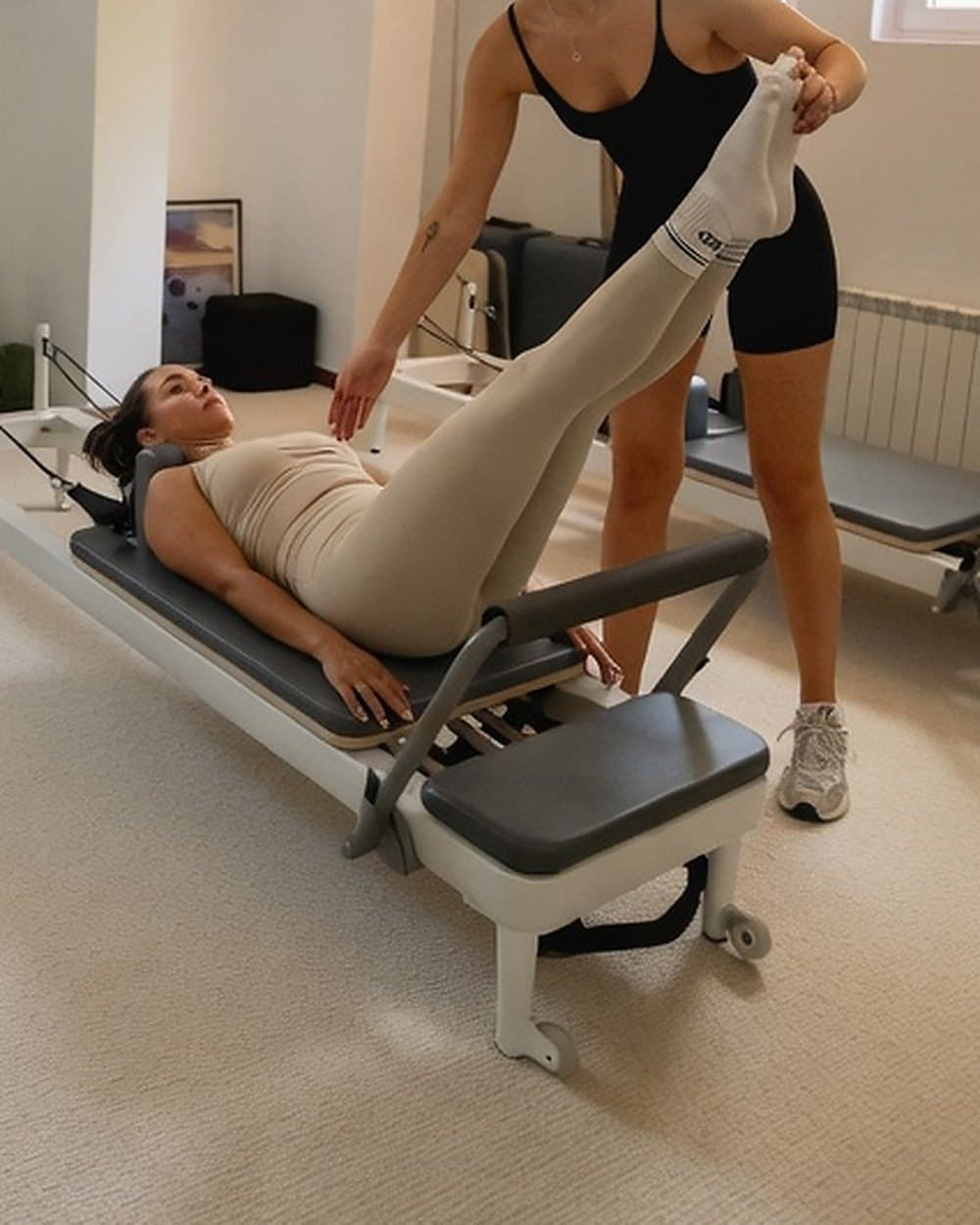 Instructoare susținând piciorul unei cliente întinse pe reformer